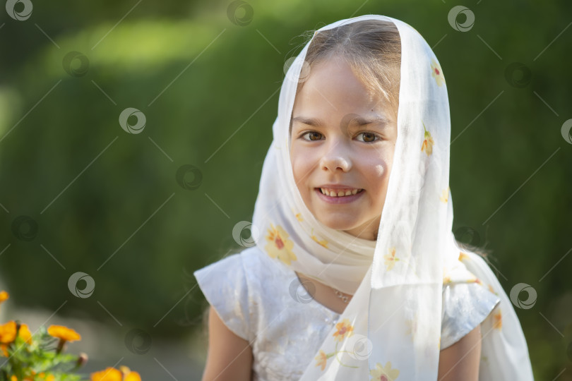 Скачать Молодая девушка в шарфе улыбается в саду при дневном свете, окруженная цветущими цветами фотосток Ozero