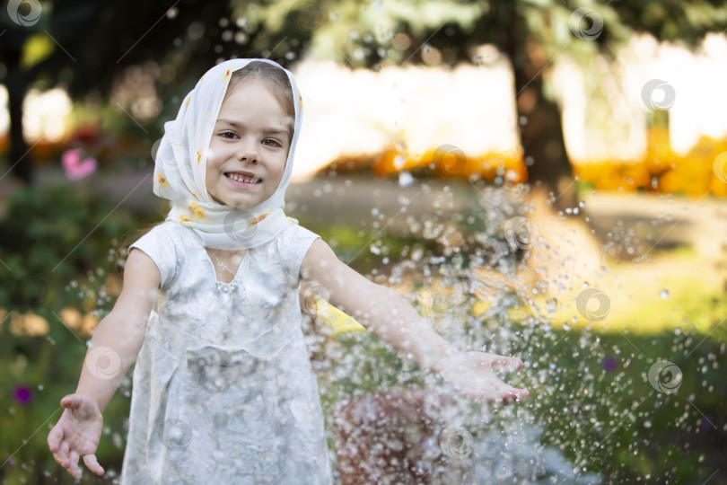 Скачать Молодая девушка в легком шарфе наслаждается брызгами воды в саду в солнечный день фотосток Ozero