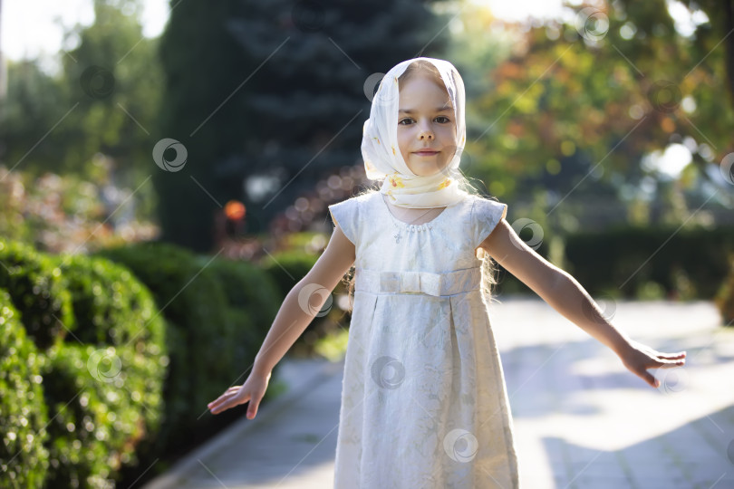 Скачать Молодая девушка в белом платье и платке наслаждается солнечным днем на садовой дорожке, окруженной зеленью фотосток Ozero