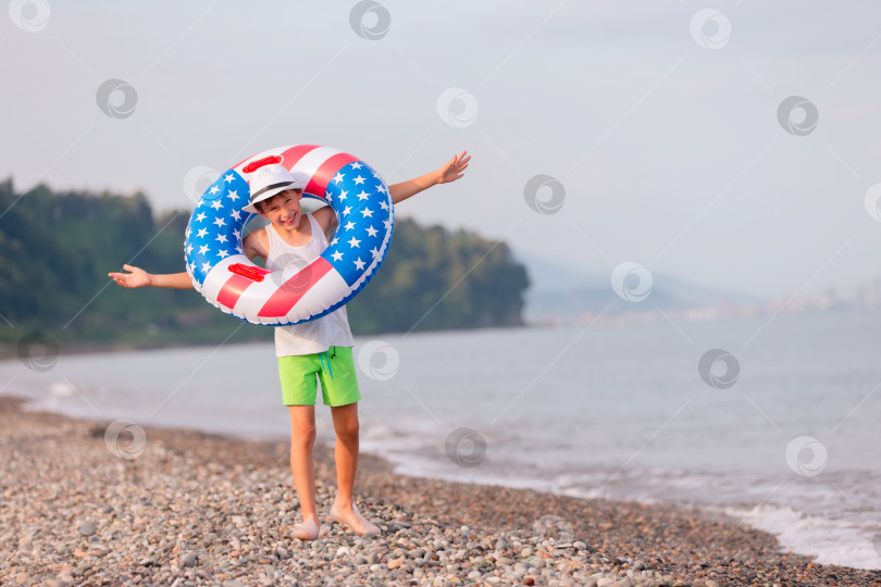Скачать Ребенок наслаждается игрой на пляже с надувным кольцом в цветах американского флага в солнечный день фотосток Ozero