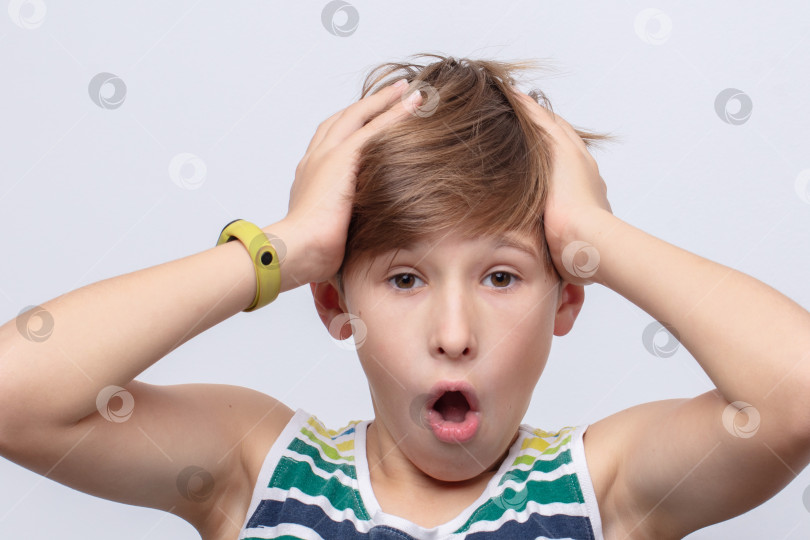 Скачать Молодой человек демонстрирует удивление и шок, положив руки на голову, в повседневной летней одежде на светлом фоне фотосток Ozero