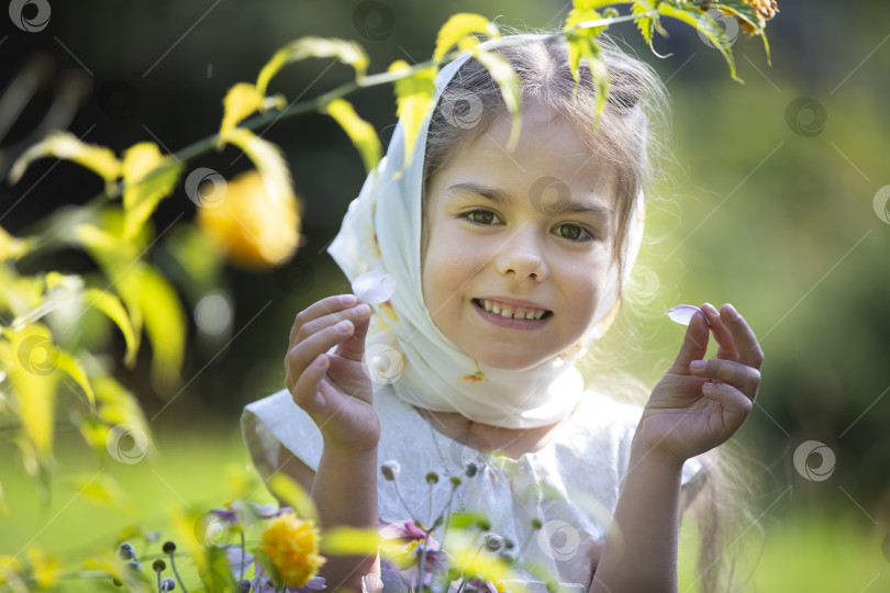 Скачать Молодая девушка улыбается, держа в руках лепестки в пышном саду солнечным днем фотосток Ozero