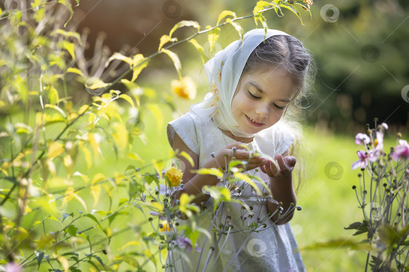 Скачать Молодая девушка в шарфе и с радостной улыбкой изучает цветы в солнечном весеннем саду фотосток Ozero