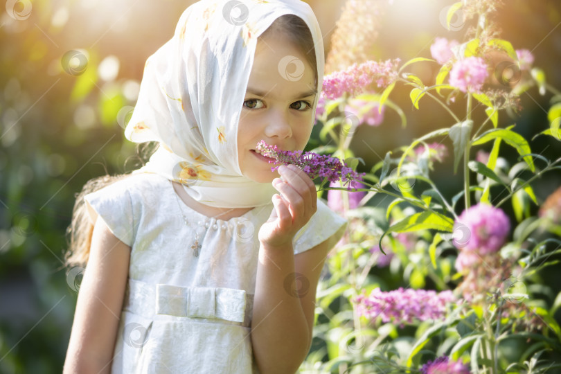Скачать Молодая девушка наслаждается цветами в залитом солнцем саду, кутаясь в шарф теплым днем фотосток Ozero