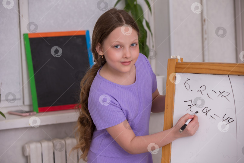 Скачать Молодая девушка радостно решает математические задачи на классной доске в светлой классной комнате фотосток Ozero