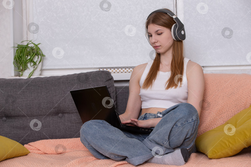 Скачать Молодая женщина работает дома за ноутбуком в наушниках в уютной обстановке гостиной фотосток Ozero