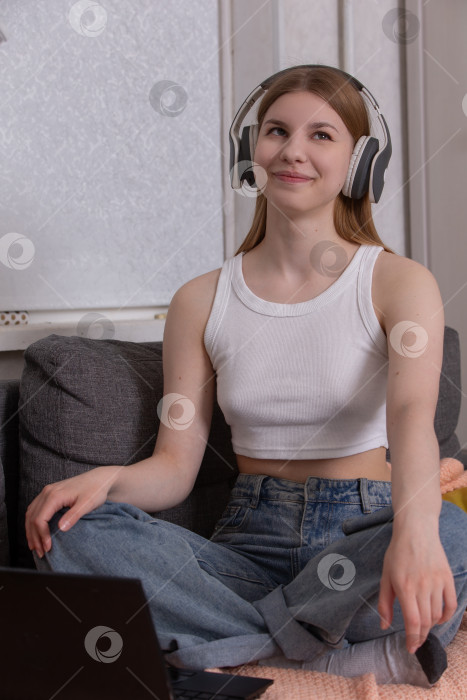 Скачать Молодая женщина наслаждается музыкой, сидя со скрещенными ногами на диване в уютном помещении с включенными наушниками фотосток Ozero