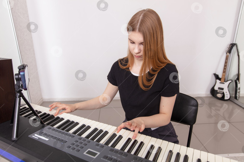 Скачать Молодая женщина играет на клавишных в яркой музыкальной студии, сосредоточившись на своем выступлении фотосток Ozero