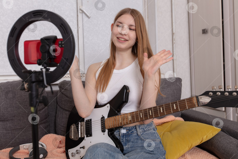 Скачать Молодая женщина ведет прямую трансляцию музыкального сеанса, играя на гитаре в уютной обстановке гостиной фотосток Ozero