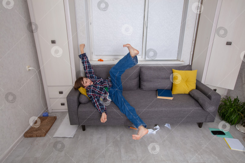 Скачать Ребенок, играючи падающий с дивана в захламленной гостиной фотосток Ozero