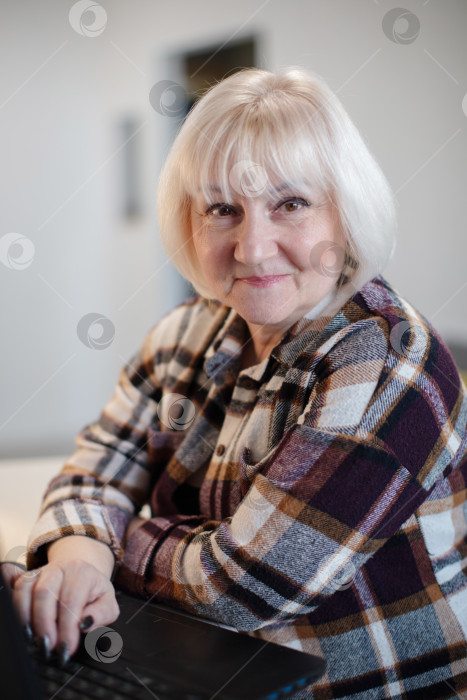 Скачать Пожилая женщина работает за ноутбуком в уютном помещении в дневное время фотосток Ozero