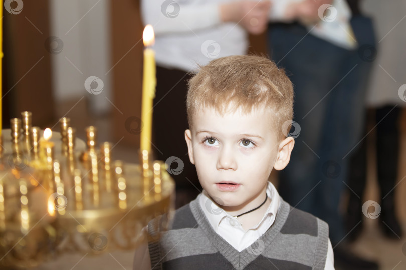 Скачать 29 сентября 2023 года, Беларусь. Город Речица. Православная церковь. Мальчик наблюдает за церемонией зажжения свечей в церкви во время тихого раздумья фотосток Ozero