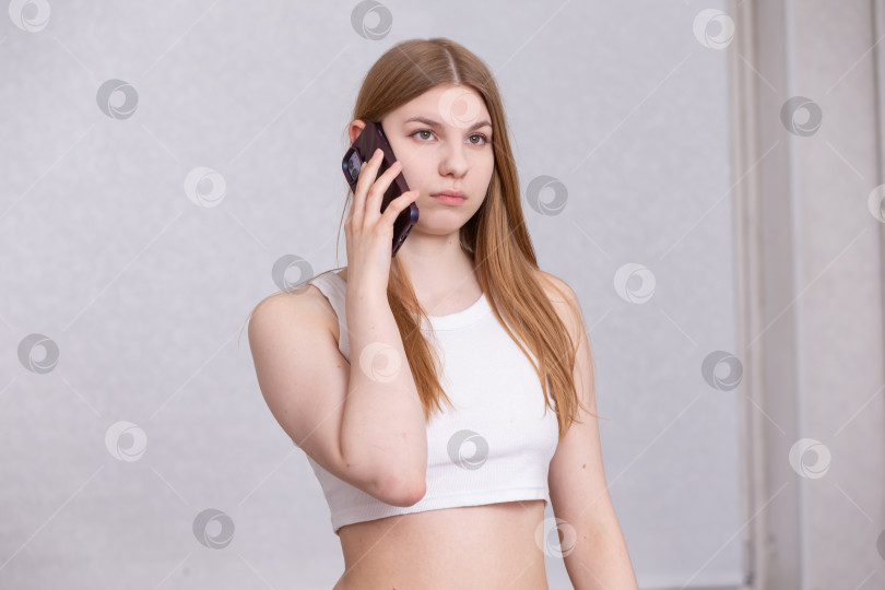 Скачать Молодая женщина стоит и разговаривает по смартфону в ярко освещенном помещении в течение обычного дня фотосток Ozero