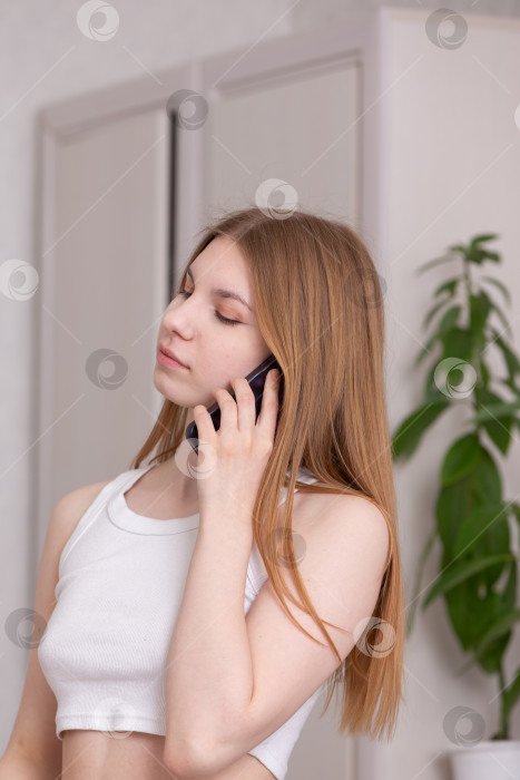 Скачать Молодая женщина разговаривает по телефону в непринужденной обстановке помещения с естественным освещением и зеленью фотосток Ozero