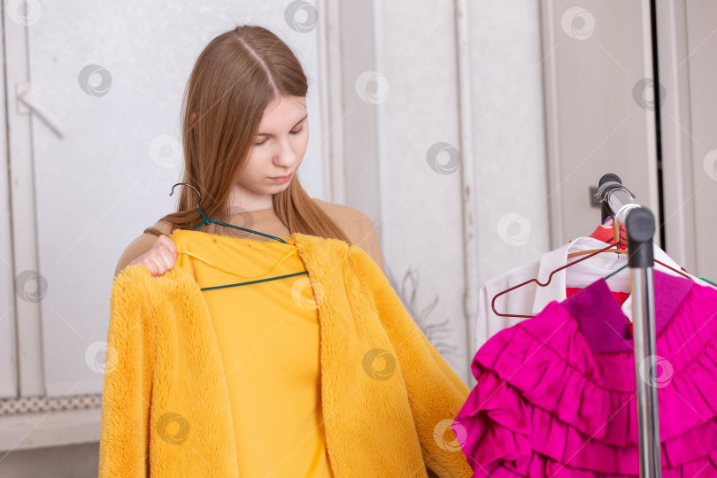 Скачать Молодая женщина выбирает между желтым жакетом и розовым платьем в уютной примерочной фотосток Ozero