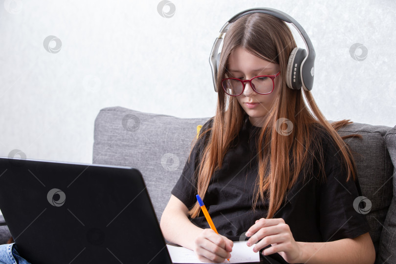 Скачать Студент занимается онлайн-обучением, делая заметки дома в наушниках в уютной обстановке фотосток Ozero