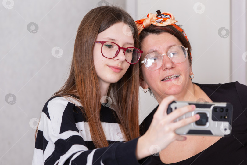 Скачать Две женщины делают совместное селфи в помещении, наслаждаясь моментом единения и смеха в уютной обстановке фотосток Ozero