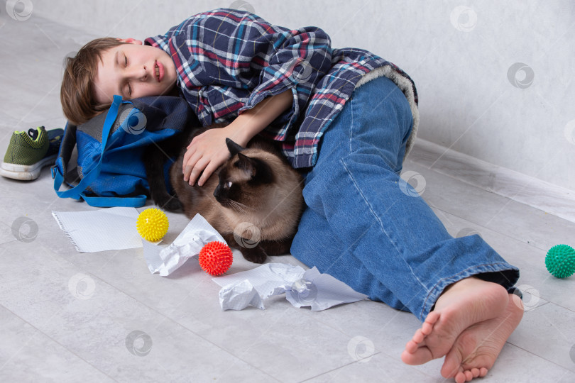Скачать Маленький мальчик лежит на полу и отдыхает с кошкой в окружении разноцветных игрушек и мятой бумаги в уютной домашней обстановке фотосток Ozero