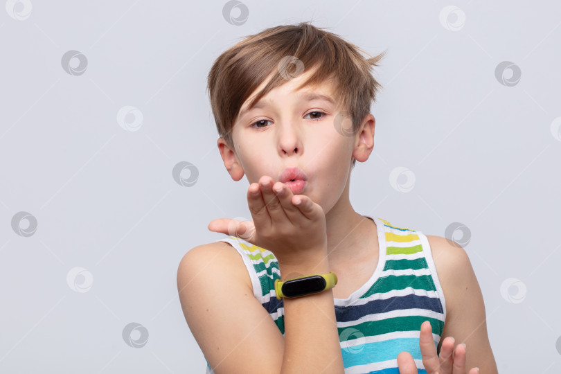 Скачать Молодой человек, одетый в полосатую майку и умные часы, посылает воздушный поцелуй на простом фоне фотосток Ozero