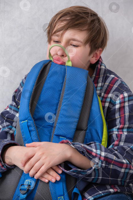 Скачать Школьник с досадой прижимает к себе холодный рюкзак и гримасничает. фотосток Ozero