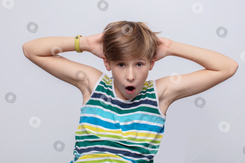 Скачать Удивленный мальчик, демонстрирующий волнение, сидит на простом фоне в повседневной полосатой майке фотосток Ozero