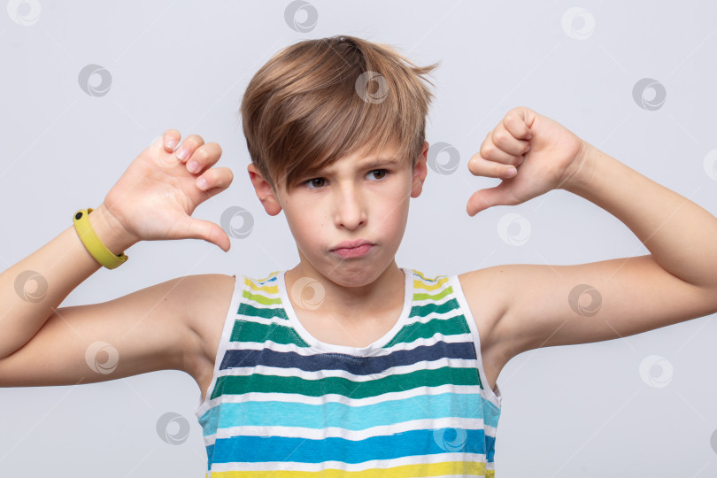 Скачать Маленький мальчик выражает разочарование жестом большого пальца, опущенного вниз, на светлом фоне фотосток Ozero