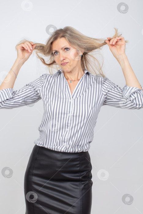 Скачать Женщина с длинными волосами, игриво теребящая пряди, позирует в стильном наряде на нейтральном фоне фотосток Ozero