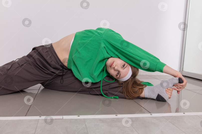 Скачать Любитель йоги утром в современном тренажерном зале в зеленой толстовке с капюшоном делает глубокую растяжку фотосток Ozero