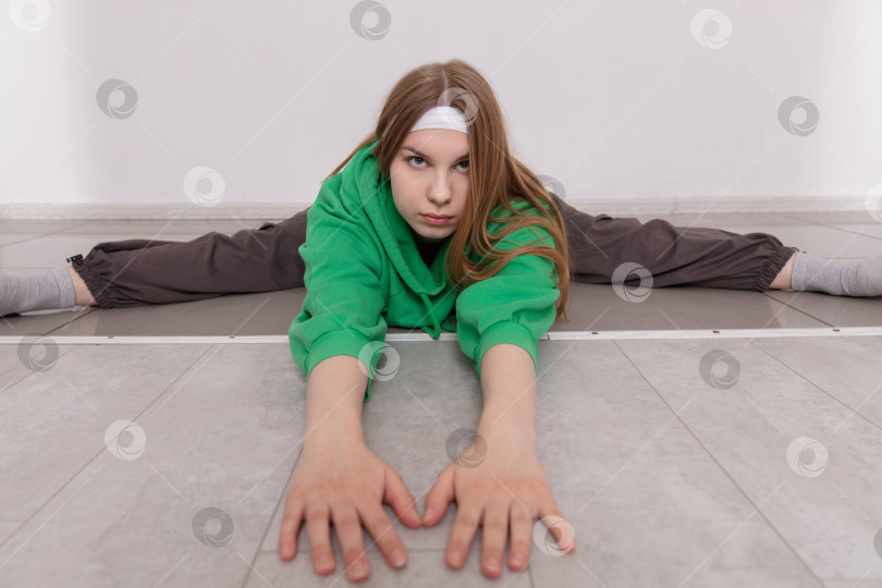 Скачать Молодая девушка тренируется на гибкость и растяжку на полу в минималистичном помещении во время утренней тренировки фотосток Ozero