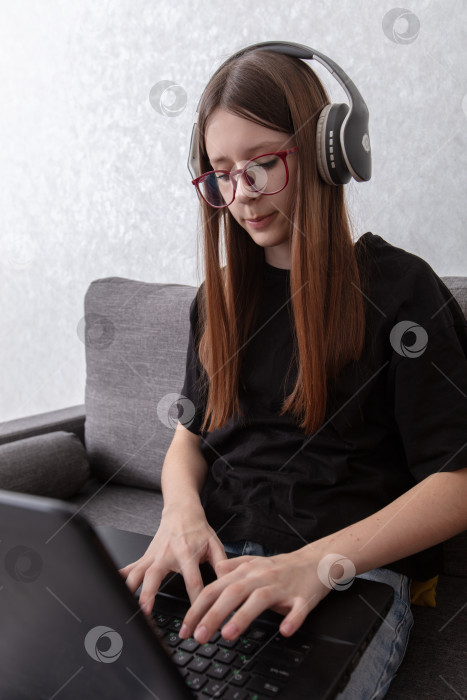 Скачать Молодая женщина работает дома с ноутбуком в наушниках в непринужденной обстановке фотосток Ozero