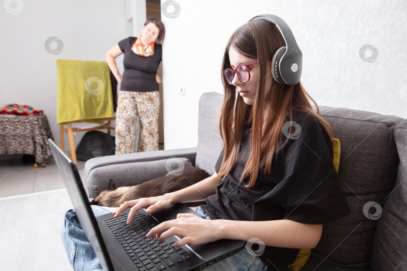 Скачать Подросток сосредоточен на онлайн-активности, в то время как взрослый наблюдает за происходящим дома, в уютном жилом пространстве фотосток Ozero