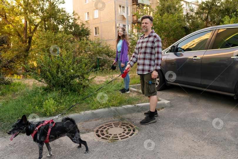 Скачать Отец и дочь выгуливают собаку на поводке возле припаркованного автомобиля фотосток Ozero