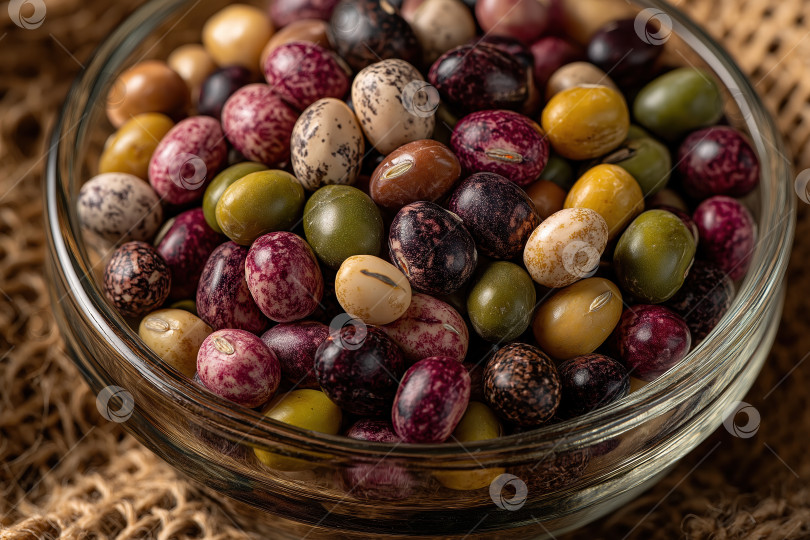 Скачать Красочный ассортимент различных сушеных бобов в стеклянной миске на фоне натуральных волокон фотосток Ozero