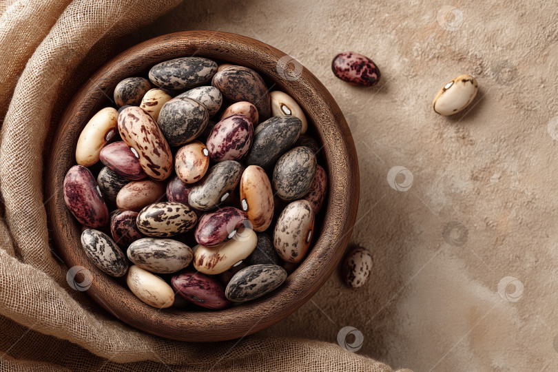 Скачать Деревянная миска, наполненная разнообразными разноцветными сушеными бобами, стоит на мягкой ткани на нейтральном фоне фотосток Ozero
