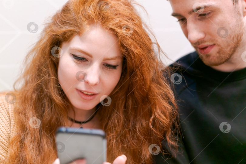 Скачать Рыжеволосая женщина смотрит в сотовый телефон фотосток Ozero