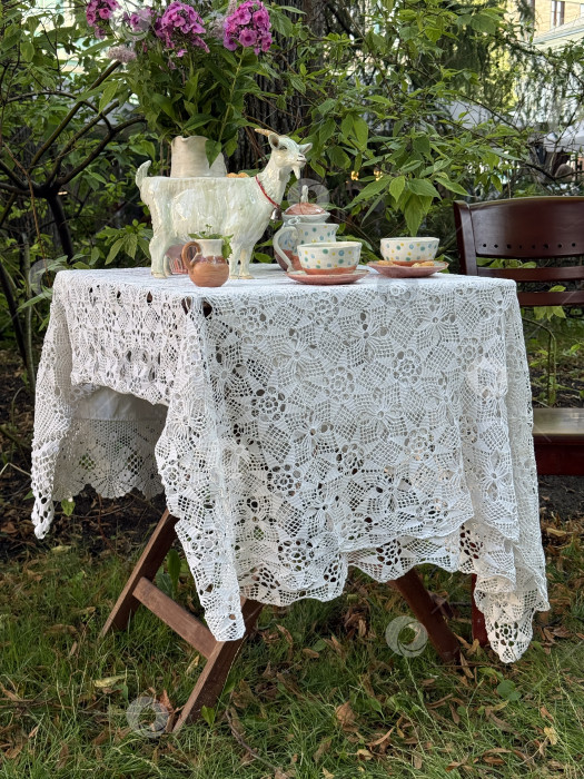 Скачать Кружевная скатерть, накинутая на стол с чайником и чашками в садовой обстановке фотосток Ozero