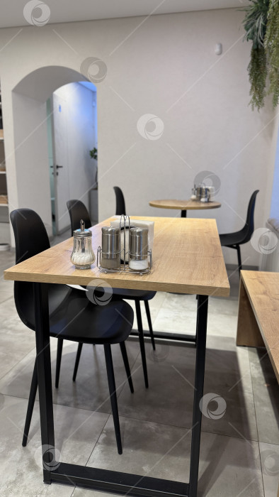 Скачать Современный интерьер кафе с деревянными столами и черными стульями, минималистичным дизайном и уютной атмосферой фотосток Ozero