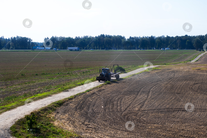 Скачать Большой трактор уверенно едет по грунтовой дороге в открытом поле фотосток Ozero