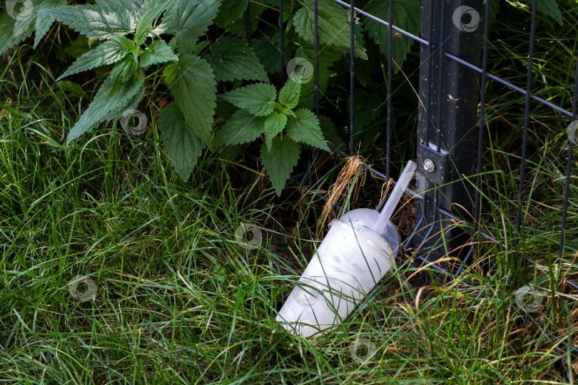 Скачать Белая чашка с соломинкой стоит в траве у столба забора фотосток Ozero