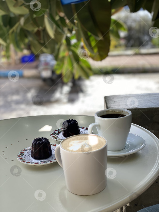 Скачать Кофейные чашки на столике кафе на открытом воздухе с выпечкой канеле, солнечный день, расслабляющая атмосфера фотосток Ozero