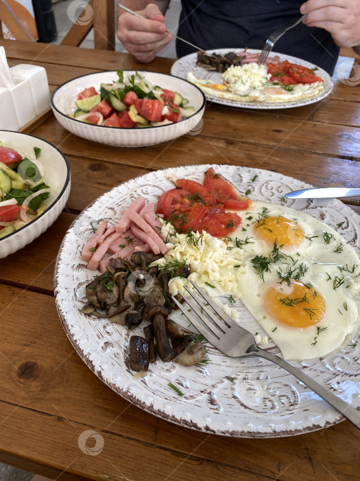 Скачать Стол для завтрака с яичницей-глазуньей, грибами, ветчиной, салатом и нарезанными помидорами на деревянной поверхности фотосток Ozero