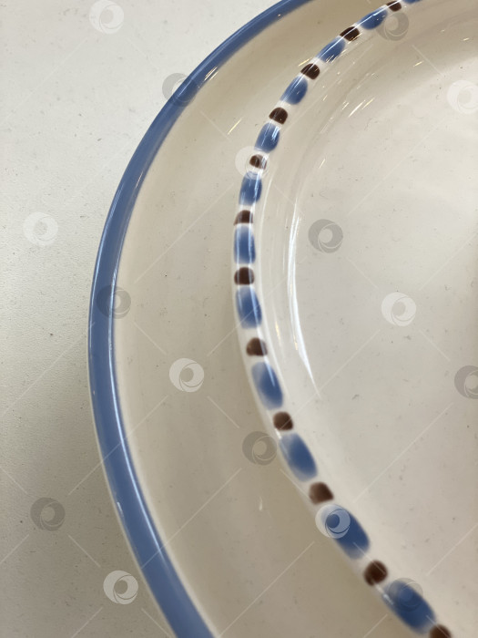 Скачать Крупный план края керамической тарелки с рисунком в синие и коричневые точки на белой поверхности, абстрактный фон фотосток Ozero