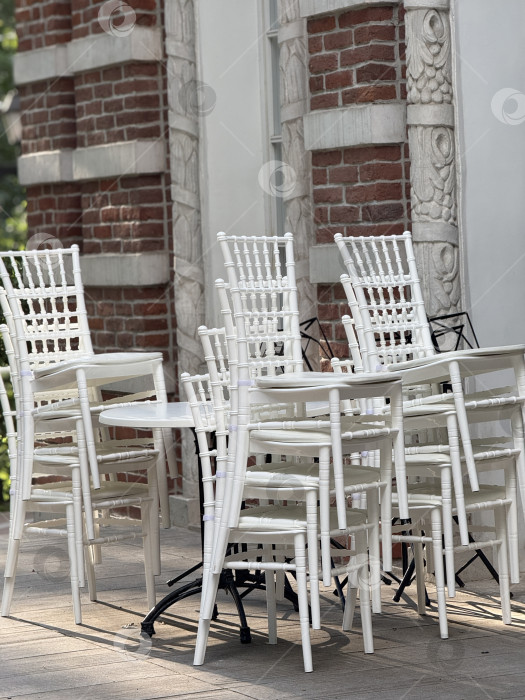 Скачать Сложенные в ряд белые стулья и столы снаружи на фоне кирпичной стены фотосток Ozero