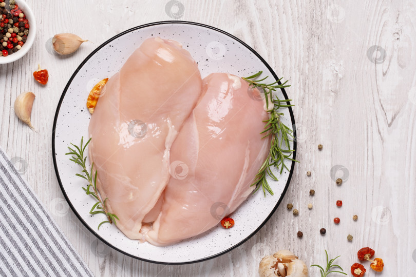 Скачать Сырая куриная грудка или филе с перцем, чесноком и свежей зеленью на белой тарелке на белом деревянном столе. Здоровое питание. Вид сверху, свободное место для копирования фотосток Ozero
