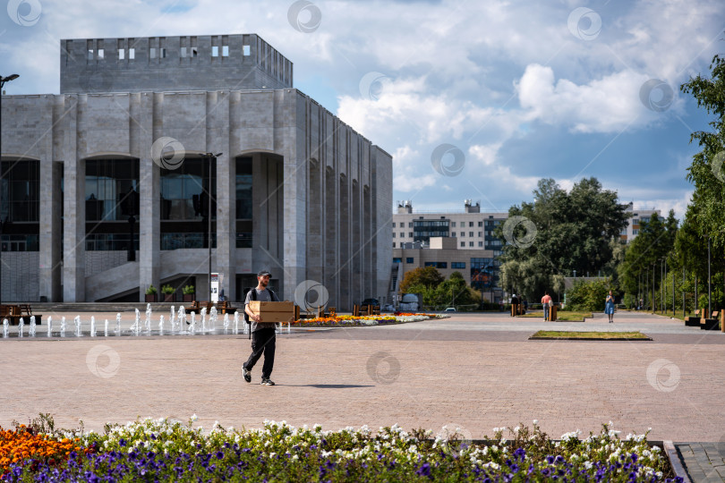 Скачать Мужчина несёт коробку на фоне здания драматического театра. Россия, Пермь, август 2025г. фотосток Ozero