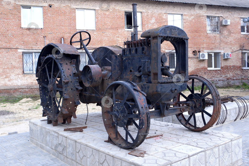 Скачать Трактор ХТЗ 15-30 1930 года выпуска Харьковского тракторного завода стоит на постаменте на фоне ветхого кирпичного дома. фотосток Ozero