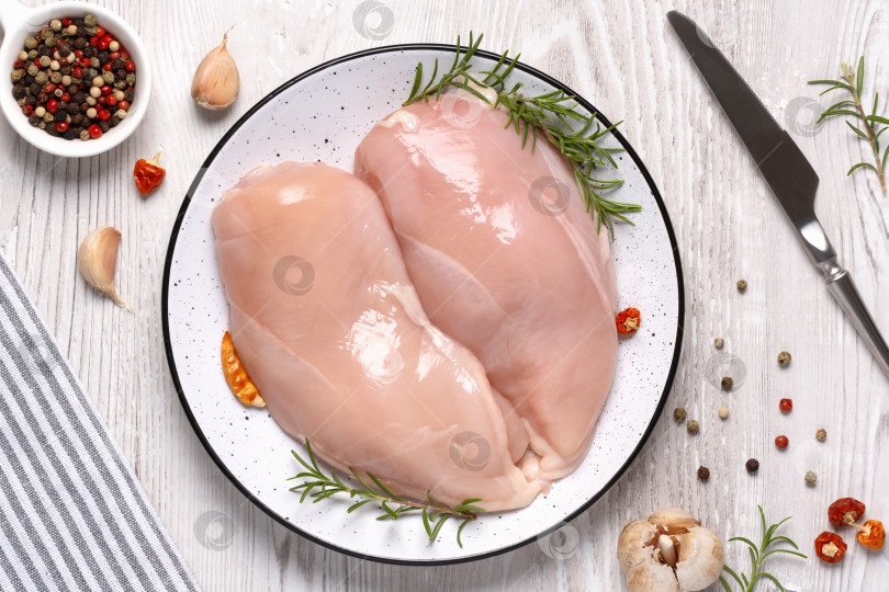 Скачать Сырая куриная грудка или филе с перцем, чесноком и свежей зеленью на белой тарелке на белом деревянном столе. Здоровое питание. Вид сверху, свободное место для копирования фотосток Ozero