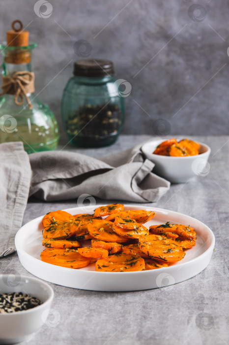 Скачать Кусочки обжаренной моркови с чесноком и зеленью на тарелке на столе в вертикальном положении фотосток Ozero