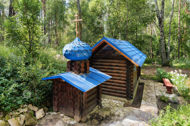 Скачать Святой источник Пресвятой Богородицы и деревянная купальня в лесу в окрестностях Клязьминского городка. Сооружения выполнены из рубленых бревен и украшены голубыми крышами. Главный домик увенчан небольшим голубым куполом с крестом. фотосток Ozero