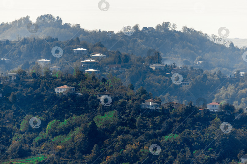 Скачать Сельская местность в Батуми. Сельские дома расположены на склонах гор. Одноэтажные, двухэтажные и трехэтажные дома окружены высокими зелеными деревьями. фотосток Ozero